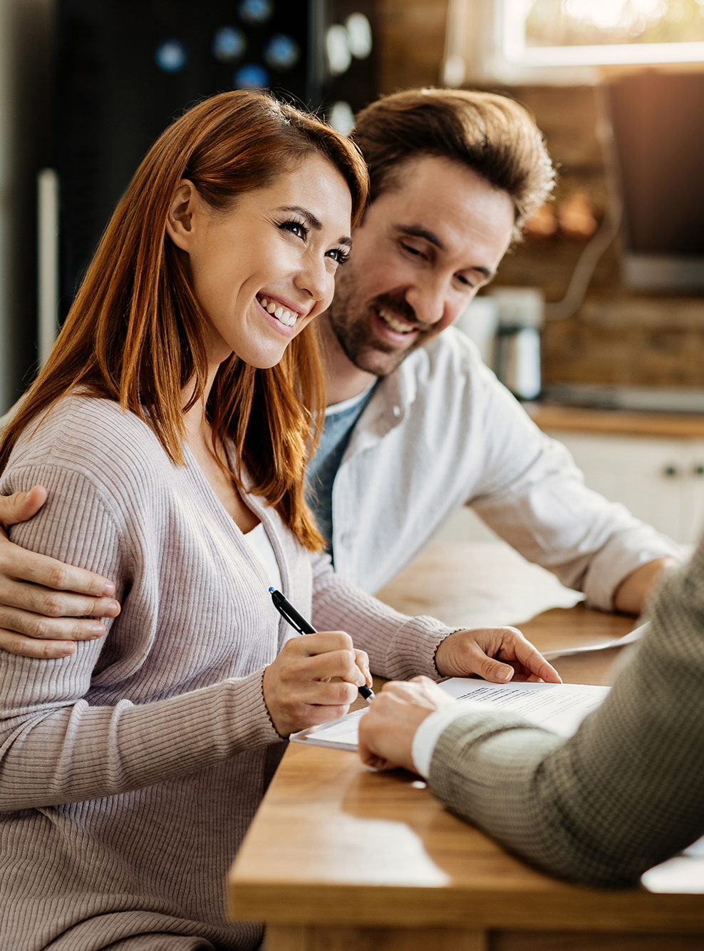 Young happy woman and her husband signing an agreement with insurance agent during a meeting.